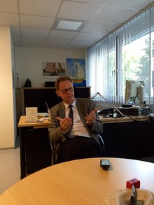 Dr. Bock sitzt im Bildzentrum am runden hellbraunen Besuchertisch seines Büros und erklärt den Verlauf einer Rehamaßnahme: auch Rentenberatung findet statt.