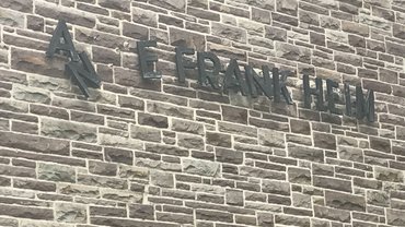 Namensschriftzug Anne Frank an einem Haus, einige Buchstabend fehlen.
