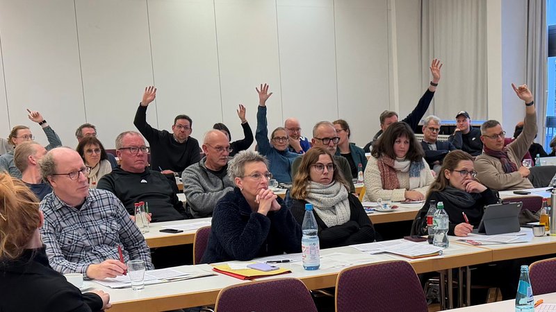 Sitzungssaal mit Menschen, die ihre Hände heben.
