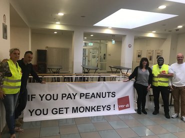 Leute vor Transparent mit der Aufschrift "If you pay peanuts you will get monkeys"