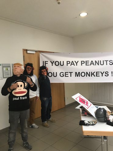 Transparent vor Eingang des Arbeitgeberberatungszimmers. Menschen mit Affenmasken davor.