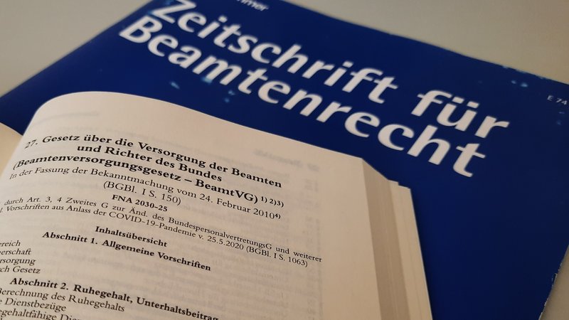 Aufgeschlagener Gesetzestext und Zeitschrift für Beamtenrecht im Hintergrund